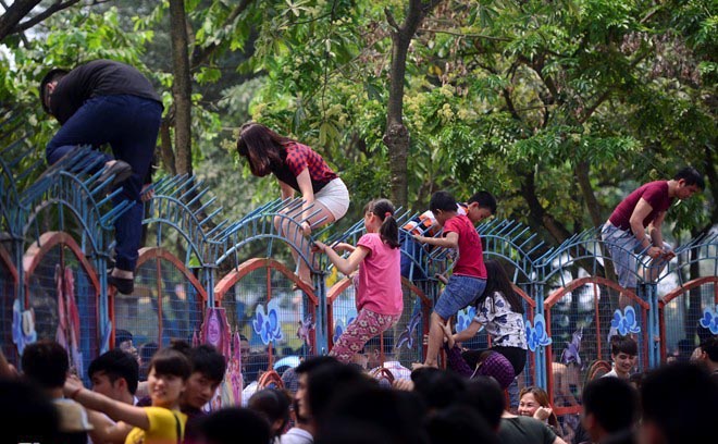 Người lớn và trẻ em thi nhau trèo rào sắt vào công viên nước.